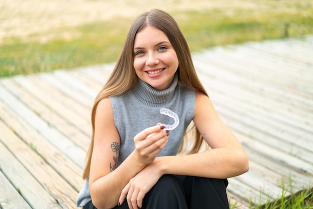 Młoda ładna blondynka trzymająca niewidoczne szelki na zewnątrz dużo się uśmiecha