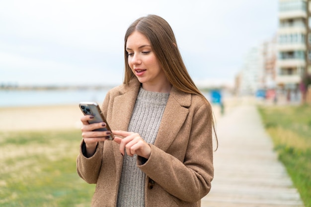 Młoda ładna Blondynka Wysyła Wiadomość Lub E-mail Za Pomocą Telefonu Komórkowego