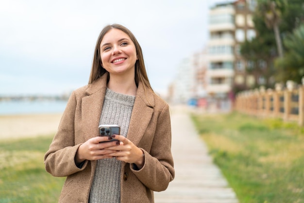 Młoda ładna blondynka za pomocą telefonu komórkowego i patrząc w górę