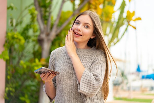 Młoda ładna blondynka za pomocą telefonu komórkowego na zewnątrz szepcząc coś