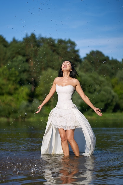 Młoda ładna brunetka kobieta w białej sukni ślubnej, spacery nad rzeką i robienia plam