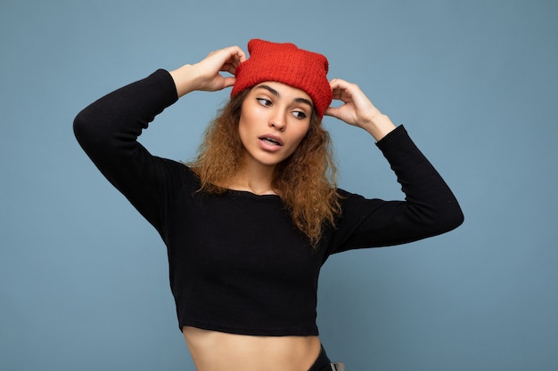 Zdjęcie młoda ładna brunetka, kręcona ze szczerymi emocjami, ubrana w stylowy czarny top i czerwony kapelusz