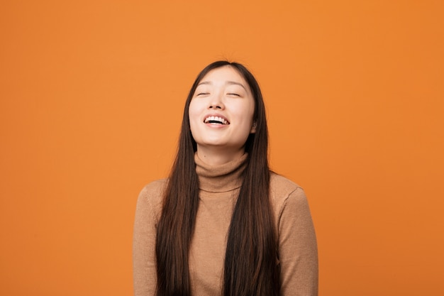 Młoda ładna Chinka zrelaksowana i szczęśliwa, śmiejąc się, wyciągając szyję pokazując zęby.