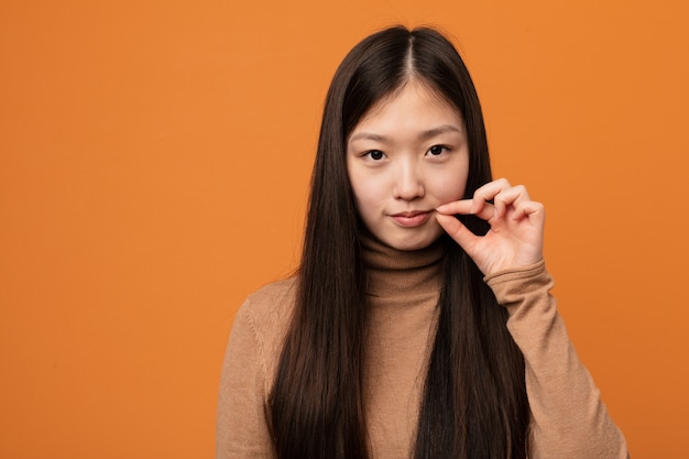 Młoda ładna chińska kobieta trzyma sekret z palcami na wargach.