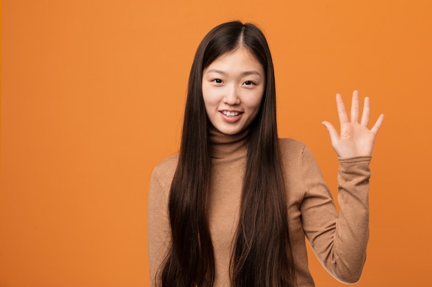 Młoda ładna chińska kobieta uśmiecha się rozochoconego seans liczba pięć z palcami.