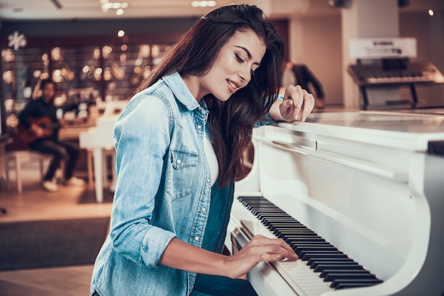 Młoda ładna dziewczyna gra na pianinie w sklepie muzycznym.