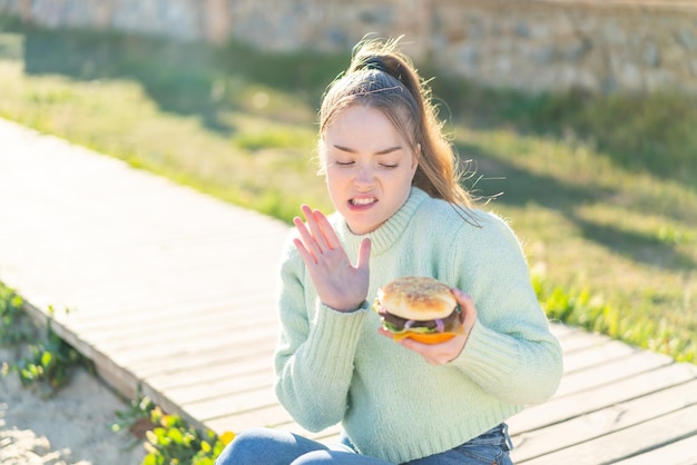 Młoda ładna dziewczyna trzyma burgera na zewnątrz