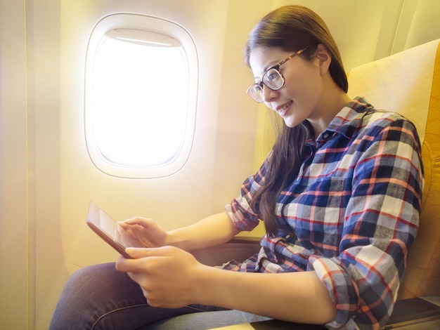 młoda ładna kobieta biznesu przy samolocie idzie do pracy i siedzi na fotelu przy oknie w promieniach słońca przy użyciu komputera przenośnego cyfrowego tabletu.