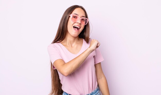 Młoda ładna kobieta czuje się szczęśliwa i staje przed wyzwaniem lub świętuje. koncepcja różowych okularów przeciwsłonecznych