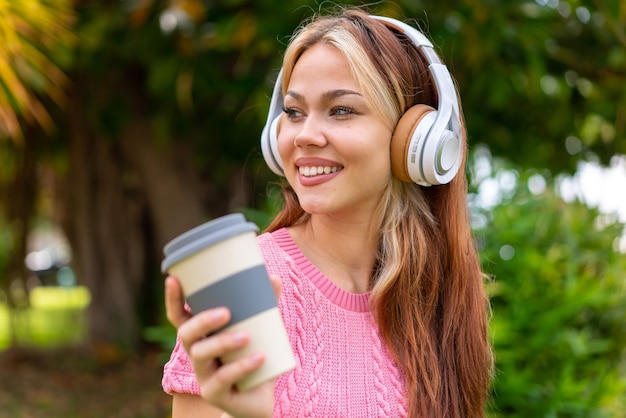 Młoda ładna kobieta na zewnątrz, słuchając muzyki i trzymając kawę na wynos