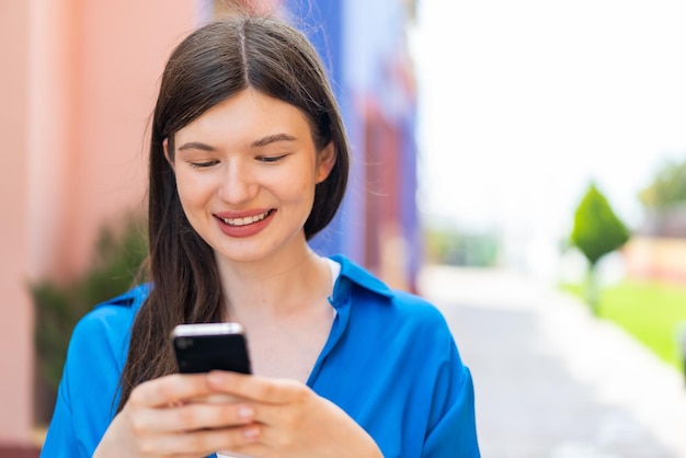 Młoda ładna kobieta na zewnątrz, wysyłając wiadomość za pomocą telefonu komórkowego