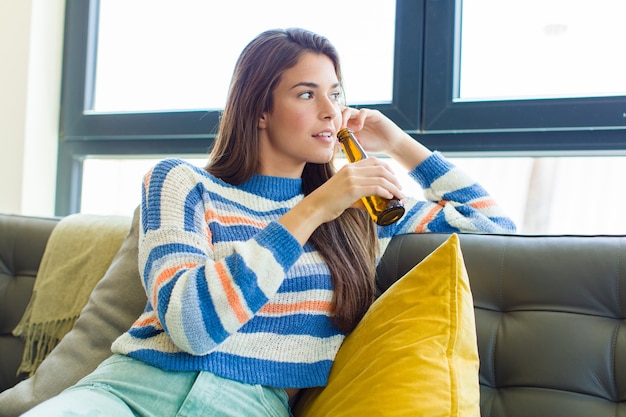 Młoda ładna kobieta o piwo siedzi na kanapie w domu shes