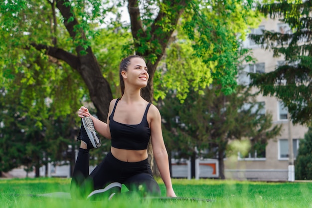 Młoda ładna kobieta, rozciąganie na matę do jogi w parku