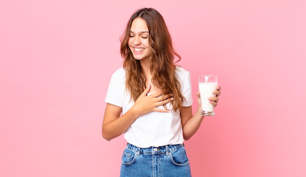 Młoda ładna kobieta śmiejąca się głośno z jakiegoś zabawnego żartu i trzymająca szklankę mleka