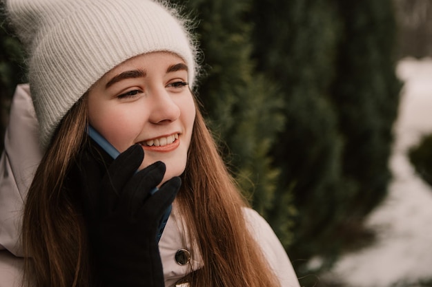 Młoda ładna kobieta świętująca ubraną ciepłą kurtkę, stojąca w pobliżu choinki, rozmawiająca przez telefon