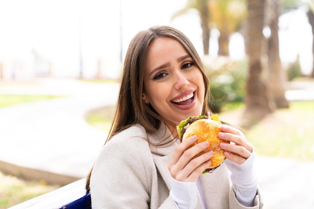 Młoda ładna kobieta trzyma burgera na zewnątrz