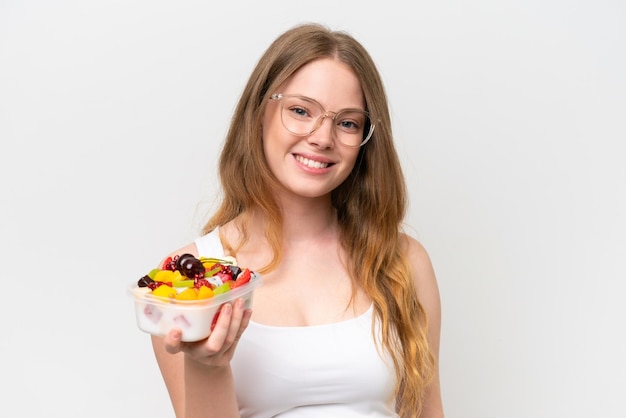 Młoda ładna kobieta trzyma miskę owoców na białym tle, uśmiechając się dużo