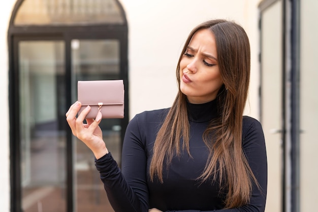 Młoda ładna kobieta trzyma portfel na zewnątrz ze smutnym wyrazem twarzy