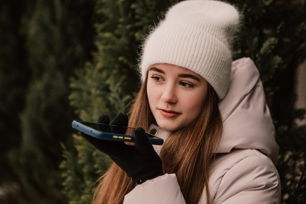 Młoda ładna kobieta ubrana w ciepłą kurtkę, stojąca w pobliżu choinki, rozmawiająca przez telefon, gestykuluje