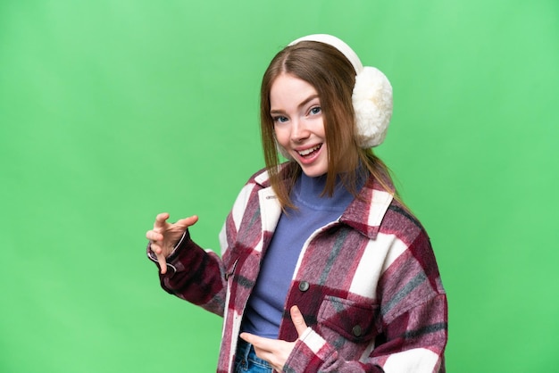 Młoda ładna kobieta ubrana w zimowe mufki na odizolowanym tle kluczowania kolorem, wykonująca gest gitary