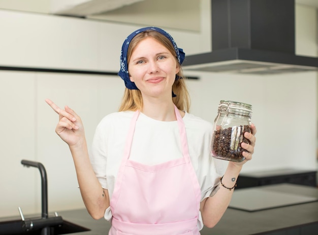 Zdjęcie młoda ładna kobieta uśmiecha się radośnie, czuje się szczęśliwa i wskazuje na bocznego szefa kuchni z ziarnami kawy