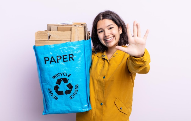 Młoda, ładna kobieta, uśmiechnięta i przyjazna, pokazująca numer pięć. koncepcja recyklingu papieru