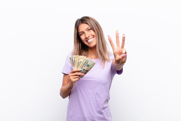 Młoda ładna kobieta uśmiechnięta i wyglądająca przyjaźnie, pokazując numer dwa lub drugi ręką do przodu, odliczając z banknotami