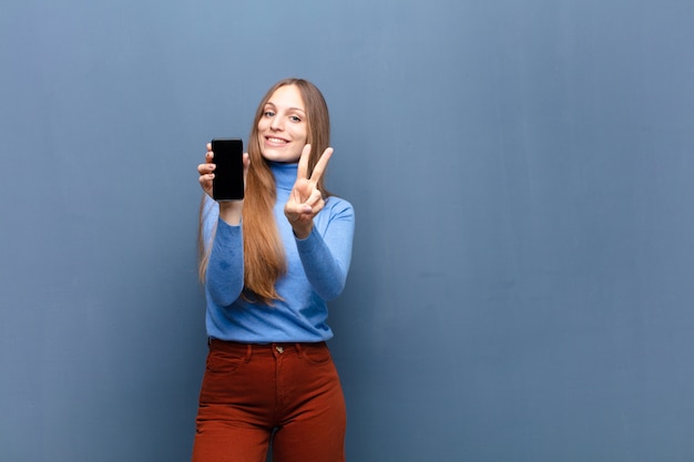 Młoda ładna kobieta używa mądrze telefon przeciw błękit ścianie z copyspace