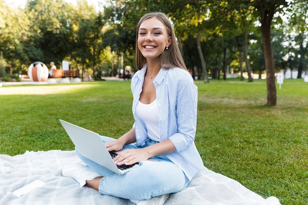 Młoda ładna kobieta w parku na zewnątrz przy użyciu komputera przenośnego.