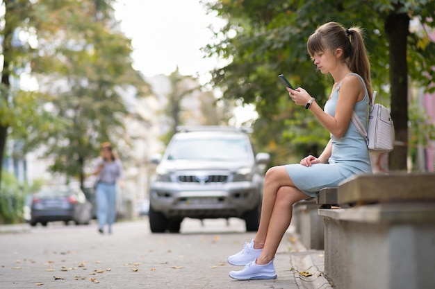 Młoda ładna Kobieta Wiadomości Na Telefon Komórkowy W Ciepły Letni Dzień, Siedząc Na Miejskiej ławce Na świeżym Powietrzu