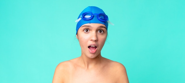 Młoda ładna kobieta wyglądająca na bardzo zszokowaną lub zaskoczoną okularami do pływania