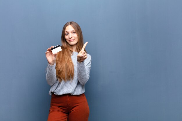 Młoda ładna kobieta z kartą kredytową przeciw błękit ścianie z odbitkową przestrzenią