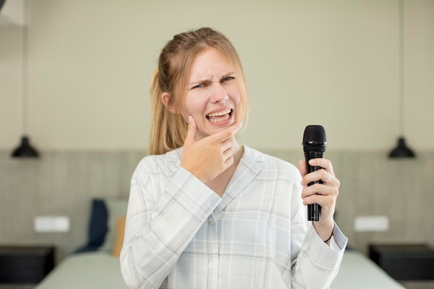 Zdjęcie młoda ładna kobieta z szeroko otwartymi ustami i oczami i ręką na mikrofonie pod brodą