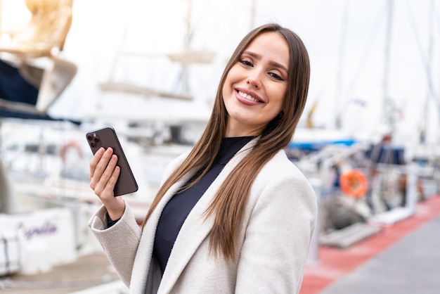 Młoda ładna kobieta za pomocą telefonu komórkowego na zewnątrz uśmiecha się dużo