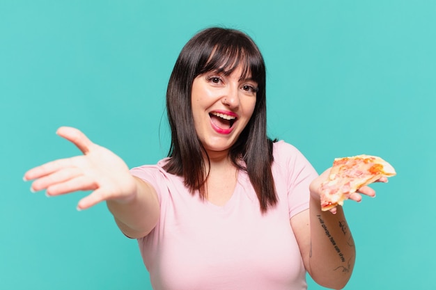 Młoda ładna krągła kobieta zaskoczona wyrazem twarzy i trzymająca pizzę