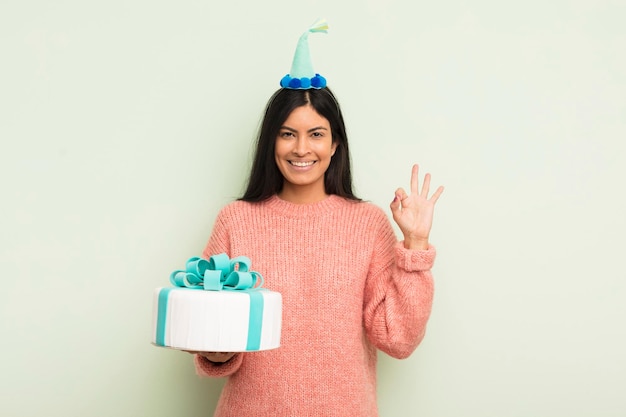 Młoda ładna latynoska kobieta czuje się szczęśliwa pokazując aprobatę z koncepcją tortu urodzinowego w porządku gest