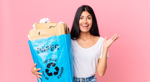 Młoda ładna latynoska kobieta czuje się szczęśliwa, zaskoczona, gdy zdaje sobie sprawę z rozwiązania lub pomysłu i trzyma papierową torbę do recyklingu