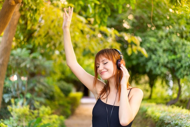 Młoda ładna ruda kobieta na zewnątrz słucha muzyki i tańczy