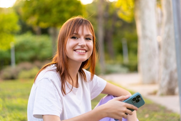 Młoda ładna ruda kobieta na zewnątrz trzymająca tablet ze szczęśliwym wyrazem twarzy