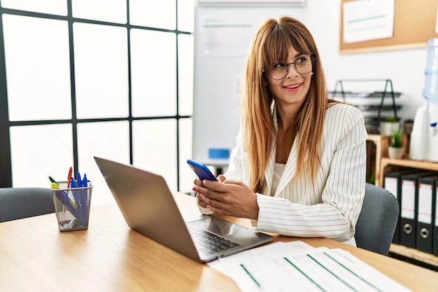 Młoda latynoska bizneswoman pracująca przy użyciu smartfona i laptopa w biurze