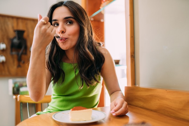 Młoda latynoska dziewczyna siedzi w kawiarni jedząc ciasto