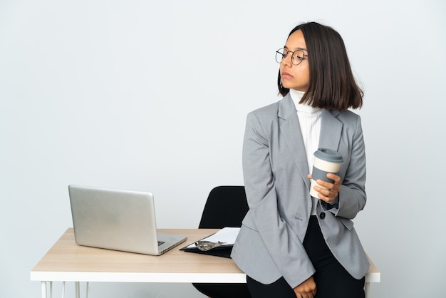 Młoda latynoska kobieta biznesu pracująca w biurze na białym tle patrząc w bok