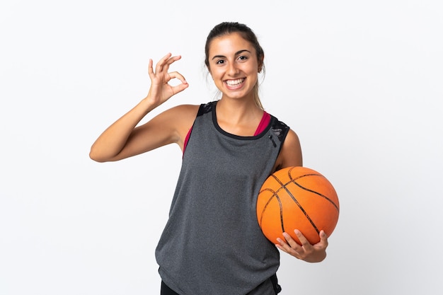 Młoda latynoska kobieta grająca w koszykówkę na białym tle pokazując znak ok palcami
