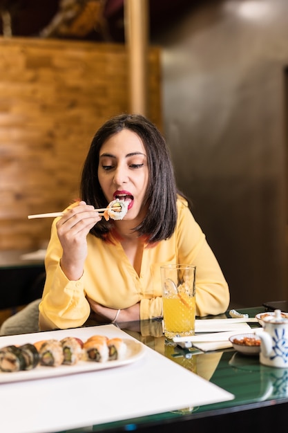 Młoda latynoska kobieta je sushi w japońskiej restauracji z jedzeniem Stylowa kolacja dla niezależnych i pewnych siebie przyjaciół spożywających zdrową żywność Kolor żółty i lawendowy 2021 rok