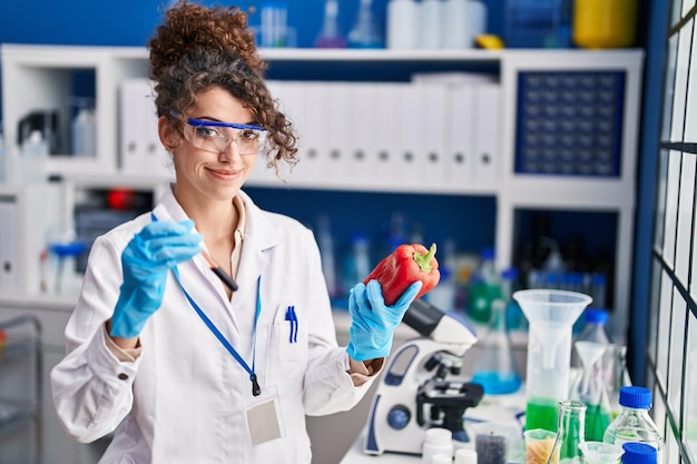 Młoda latynoska kobieta naukowiec trzymająca analizę probówki krwi i czerwoną paprykę w laboratorium