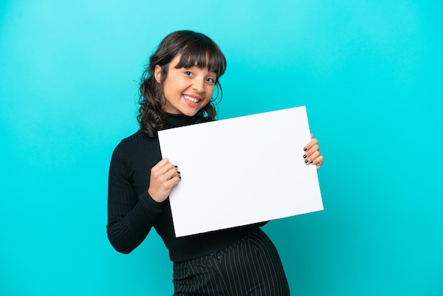 Młoda latynoska kobieta odizolowana na niebieskim tle trzymająca pustą afisz z szczęśliwym wyrazem twarzy