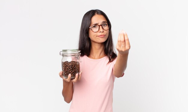 Młoda latynoska kobieta robi gest kaprysu lub pieniędzy, mówiąc, że masz zapłacić i trzymając butelkę ziaren kawy