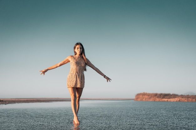 Młoda latynoska kobieta spacerująca lub pozująca na wodzie z otwartymi ramionami o zachodzie słońca