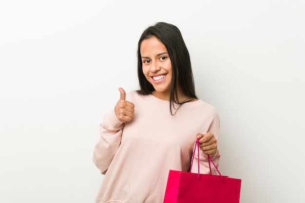 Młoda latynoska kobieta trzyma torba na zakupy uśmiecha się kciuk up i podnosi