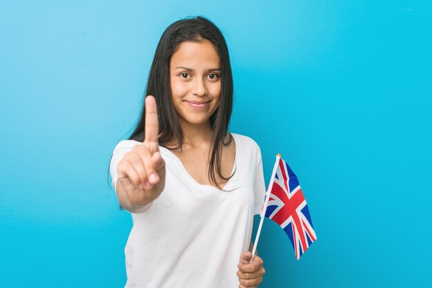 Młoda Latynoska Kobieta Trzyma Zlaną Królestwo Flaga Pokazuje Liczbę Jeden Z Palcem.